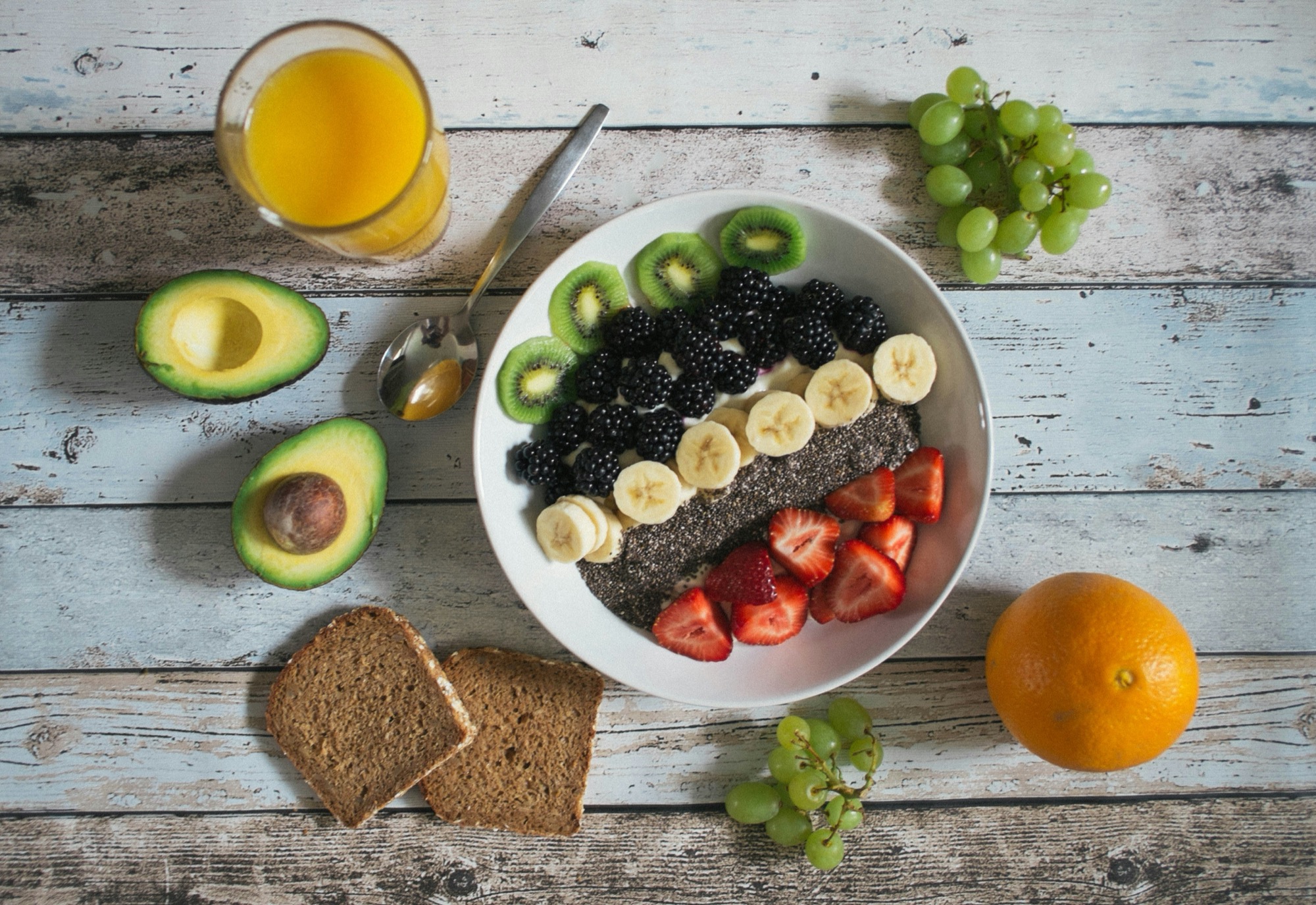 Fresh plant-forward breakfast spread with a fruit and chia bowl, avocado, whole-grain toast, and orange juice